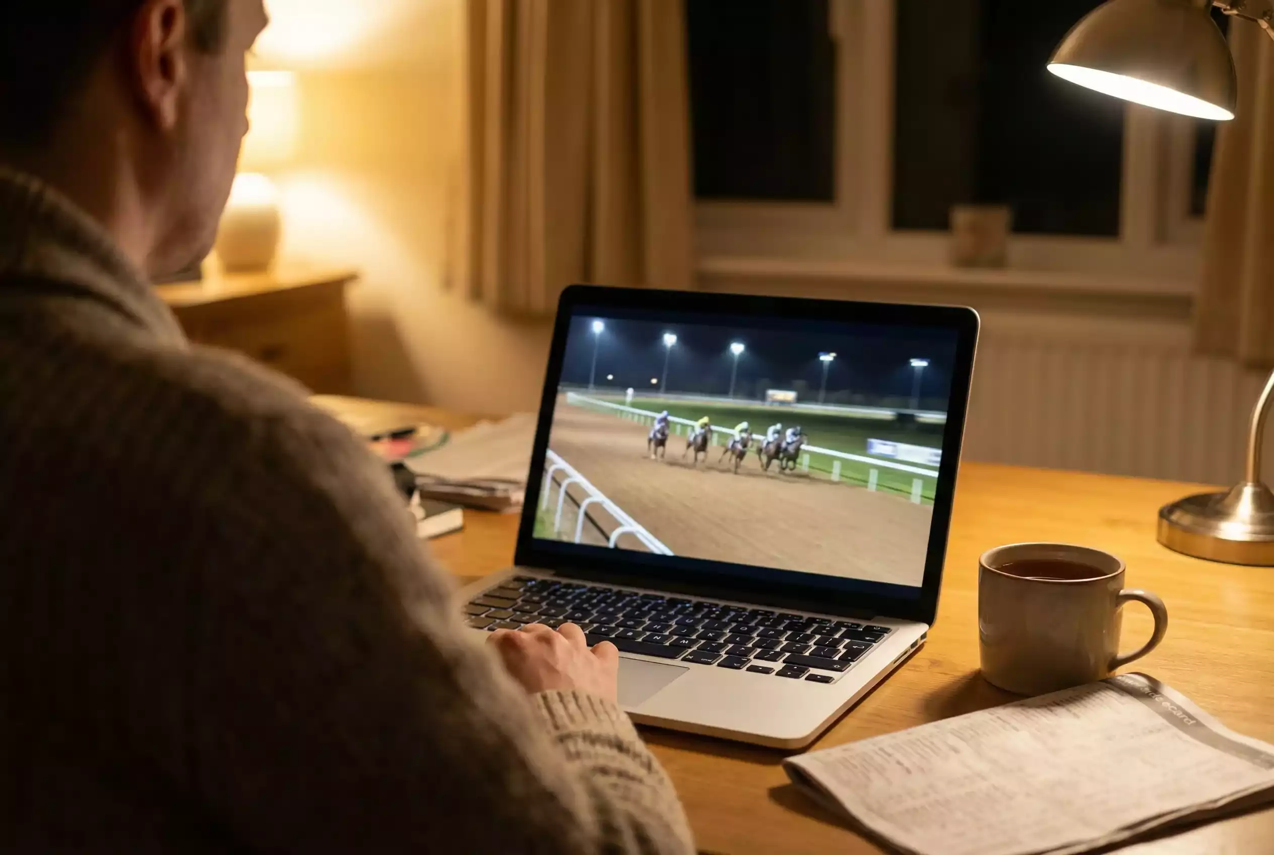 Person watching a live horse race stream on a screen with a racecard nearby
